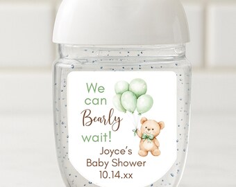 May include: A clear hand sanitizer bottle with a white cap and a label featuring a teddy bear holding balloons. The label reads "We can bearly wait!" and includes baby shower details. The bottle is decorated with small, glittery specks.