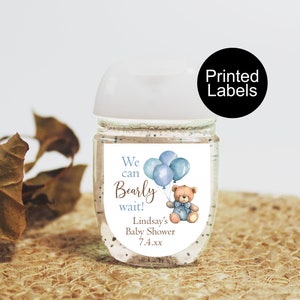 May include: A clear hand sanitizer bottle with a white top and a label featuring a teddy bear, balloons, and the text "We can bearly wait!" for Lindsay's Baby Shower. The label is accented with blue and brown watercolor illustrations.