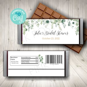 May include: A white chocolate bar wrapper with a green watercolor floral design. The text "Julie's Bridal Shower" and "October 23, 2022" is printed in gold. The back of the wrapper has a nutrition facts label and a barcode.