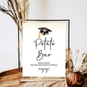 May include: A framed sign with the words "Potato Bar" in elegant script, topped with a graduation cap illustration. The sign includes the text "Grab a potato and add your favorite toppings, enjoy!" and is set against a gold glitter background.