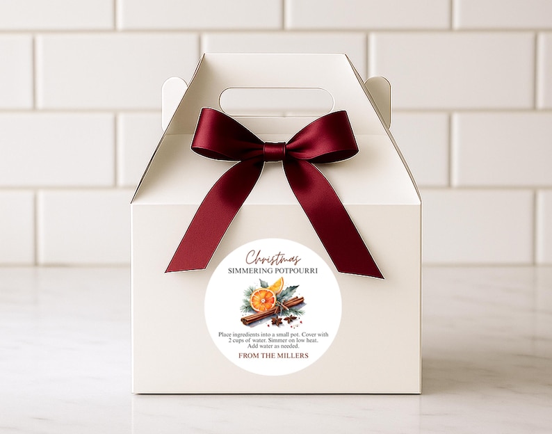 May include: A white gift box tied with a burgundy bow. The front features a round sticker with "Christmas Simmering Potpourri", instructions, and a watercolour illustration of orange slices and cinnamon sticks.