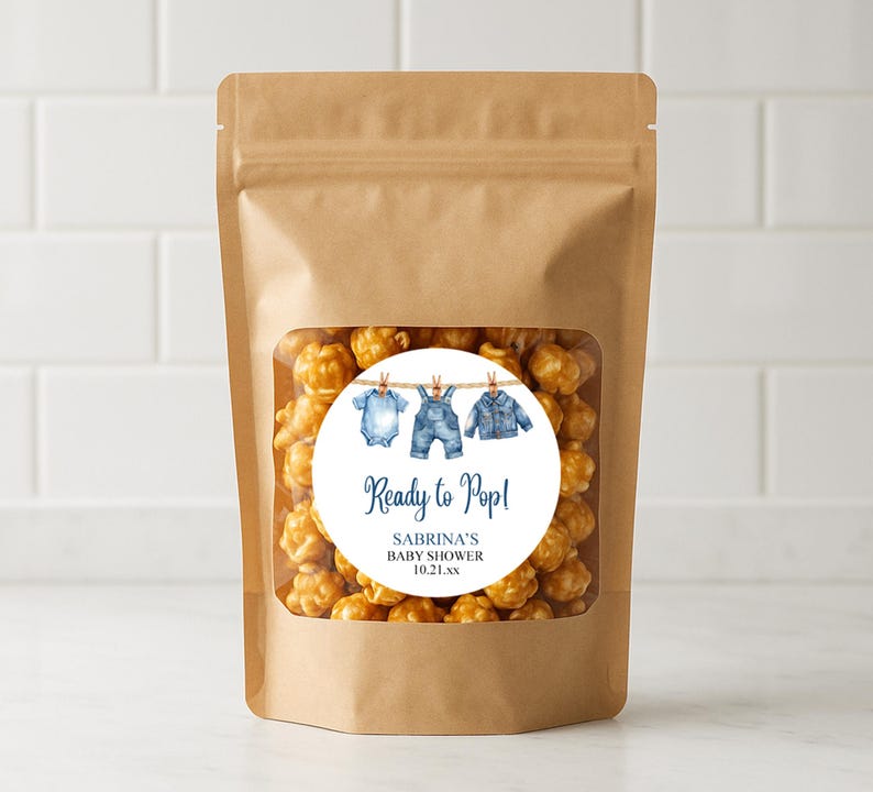 May include: A brown paper bag with a clear window filled with caramel popcorn. A round sticker on the bag reads "Ready to Pop!" with baby clothes illustrations and the text "Sabrina's Baby Shower 10.21.xx".