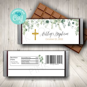 Puede incluir: Envoltorio de barra de chocolate blanco con una cruz dorada y hojas de eucalipto verdes. El envoltorio dice "Ashley's Baptism" y "October 23, 2022".