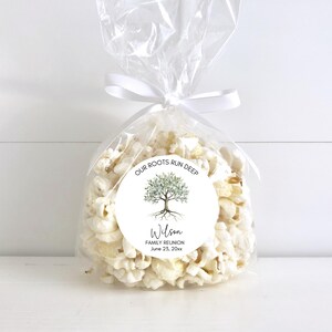 May include: A clear cellophane bag filled with popcorn, tied with a white ribbon. A round sticker on the bag features a tree illustration and the text "OUR ROOTS RUN DEEP" and "Wilson FAMILY REUNION June 23, 20xx."
