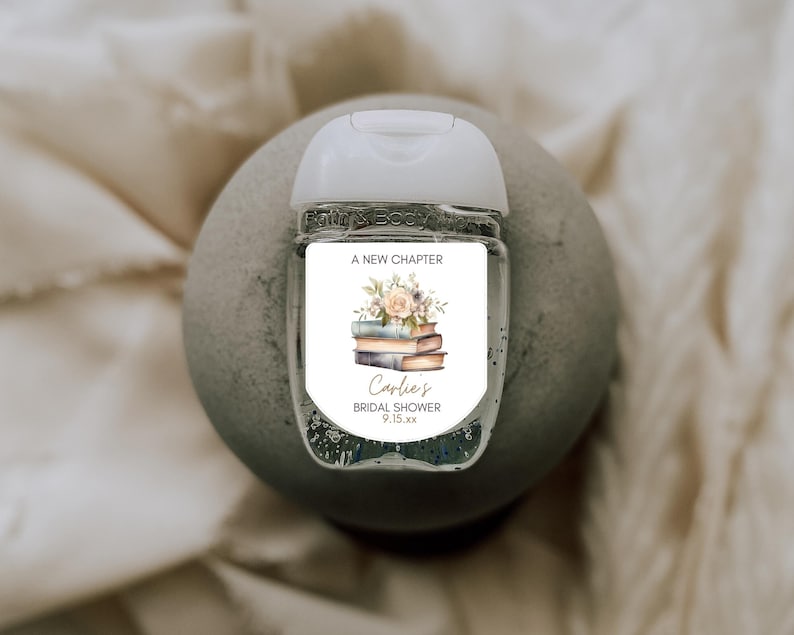 May include: A clear hand sanitizer bottle with a white cap and a label featuring a stack of books and floral elements. The label reads "A New Chapter" and "Carlie's Bridal Shower 9.15.xx".