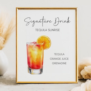 Op de afbeelding: Een ingelijste print met een gouden rand, met een aquarel illustratie van een Tequila Sunrise cocktail. De drank zit in een helder glas met een sinaasappelschijfje. Tekst luidt "Signature Drink" en "Tequila Sunrise".