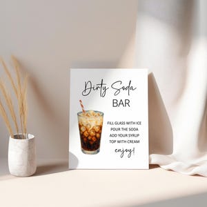 Puede incluir: Un letrero blanco con las palabras "Dirty Soda BAR" en escritura negra. Debajo, se enumeran las instrucciones para preparar una bebida. Se muestra un vaso de refresco con hielo y una pajita.