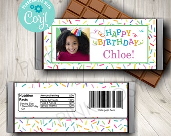Puede incluir: Un envoltorio de barra de chocolate blanco con un patrón de confeti colorido. El envoltorio tiene una foto de una niña pequeña con un sombrero de cumpleaños y el texto "¡Feliz cumpleaños Chloe!" en letras de colores. La parte posterior del envoltorio tiene una etiqueta de información nutricional y un código de barras.