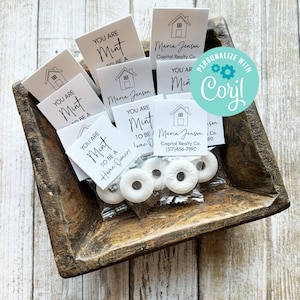 May include: A wooden tray filled with small white bags containing white mints and small white cards with the text "You are a mint to be a home owner!" and a house icon. The cards also include the name "Maria Jenson" and the text "Capital Realty Co. (517)456-7890".