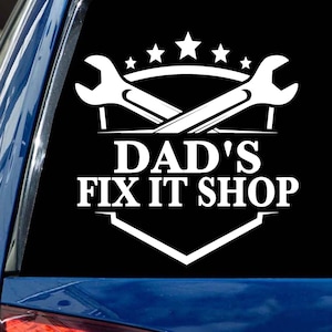 May include: White vinyl decal with two crossed wrenches and the text "DAD'S FIX IT SHOP" in a white shield shape. The wrenches are surrounded by five white stars.