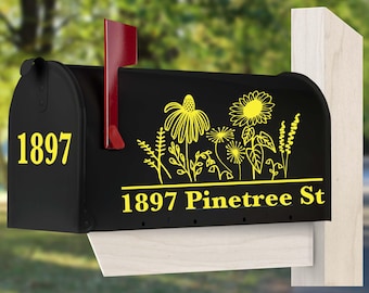 May include: A black metal mailbox featuring a red flag and yellow vinyl graphics. The front displays the number 1897, while the side shows a yellow floral design above the text 1897 Pinetree St. The mailbox is mounted on a light-colored wooden post.