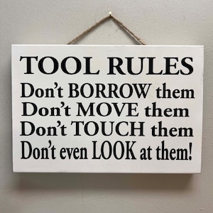 May include: White wooden sign with black text that reads "TOOL RULES Don't BORROW them Don't MOVE them Don't TOUCH them Don't even LOOK at them!"