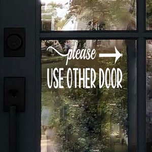 May include: A white sign on a glass door with an arrow pointing to the right and the text "Please use other door".