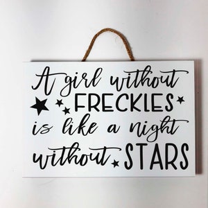 May include: White wooden sign with black text and stars that reads "A girl without *FRECKLES* is like a night without *STARS*"