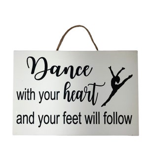 May include: White wooden sign with a black silhouette of a dancer and the text "Dance with your heart and your feet will follow."