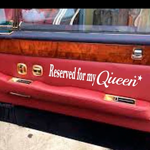 May include: A red car door panel with the text "Reserved for my Queen" in white script. The door features wood trim and gold-colored accents. The interior appears to be a luxury vehicle.