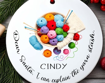 May include: White ceramic ornament with a red ribbon, featuring a basket of colorful yarn balls, knitting needles, and the text "Dear Santa, I can explain the yarn stash. CINDY."