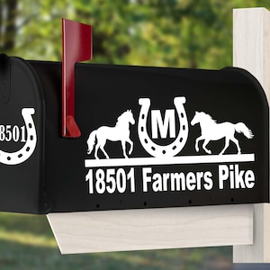 May include: A black metal mailbox featuring a red flag and white vinyl decals. The front displays a horseshoe with the number 18501. The side shows two horses flanking a horseshoe with the letter M, and the text 18501 Farmers Pike below.