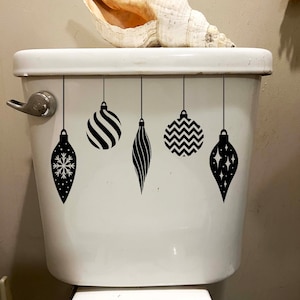 Peut inclure: Un réservoir de toilette blanc avec des autocollants d'ornements de Noël noirs et blancs. Un coquillage est posé sur le dessus du réservoir.
