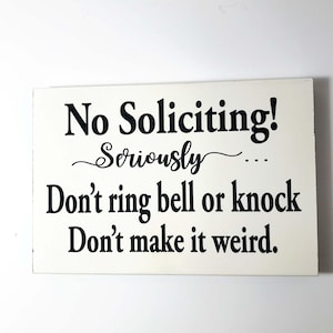 May include: White wooden sign with black text that reads "No Soliciting! Seriously... Don't ring bell or knock Don't make it weird."