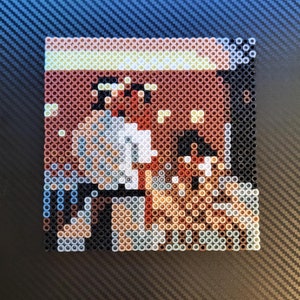 May include: A pixel art image of two people standing next to each other. The image is made of small, colorful beads. The people are wearing white shirts and brown pants. The background is a brown wall with a yellow stripe.