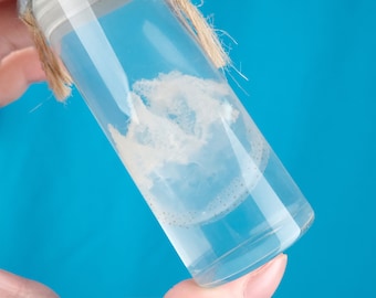 May include: A clear glass jar with a white, cloudy substance inside. The jar has a silver lid and a brown twine tied around the top.