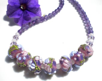 May include: A purple and pink glass bead necklace with floral designs. The necklace is made with amethyst beads and features a variety of glass beads with floral patterns.