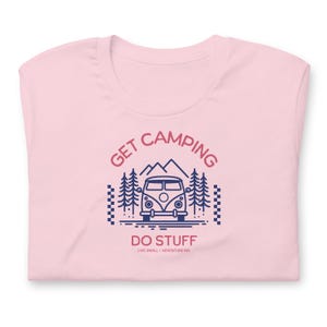 Pode incluir: Uma t-shirt rosa claro com um gr&aacute;fico azul escuro de uma carrinha de campismo, pinheiros e montanhas. O texto diz GET CAMPING DO STUFF e LIVE SMALL + ADVENTURE BIG. O design inclui um padr&atilde;o de xadrez nos lados esquerdo e direito.