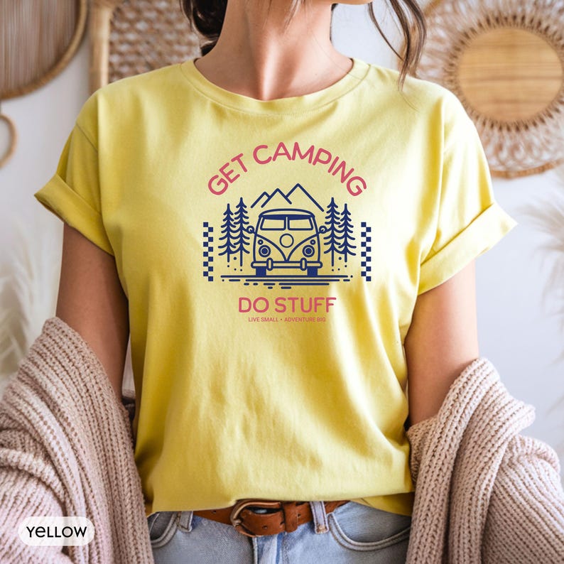 Pode incluir: Uma t-shirt amarela de manga curta com um gr&aacute;fico azul escuro de uma carrinha de campismo, pinheiros e montanhas. O texto diz GET CAMPING em rosa, DO STUFF em rosa e LIVE SMALL ADVENTURE BIG em letras pequenas cor-de-rosa abaixo do gr&aacute;fico.