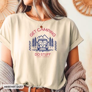 Pode incluir: Uma t-shirt de cor creme com uma impress&atilde;o gr&aacute;fica de uma carrinha azul, pinheiros e montanhas. O texto diz GET CAMPING em rosa, DO STUFF em rosa e LIVE SMALL + ADVENTURE BIG em letras pretas mais pequenas. A t-shirt est&aacute; rotulada como HEATHER DUST.