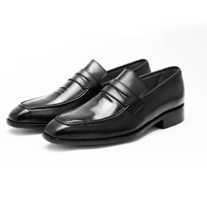 Puede incluir: Un par de mocasines de cuero negro con un dise&ntilde;o sencillo. Los mocasines tienen una punta puntiaguda y una sola correa sobre el empeine.