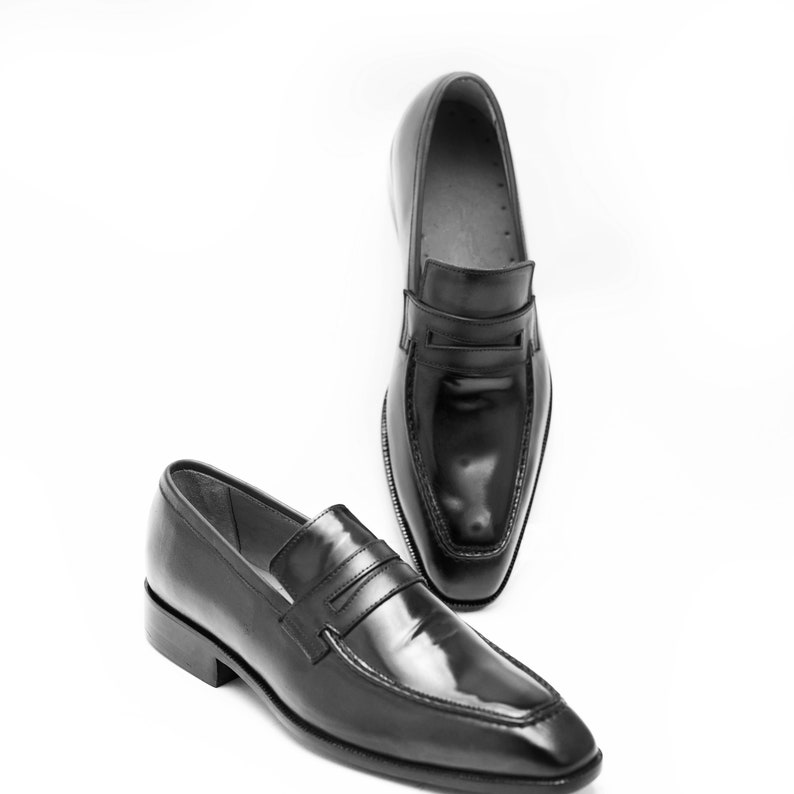 Puede incluir: Dos mocasines de cuero negro con punta puntiaguda y una sola correa en la parte superior.