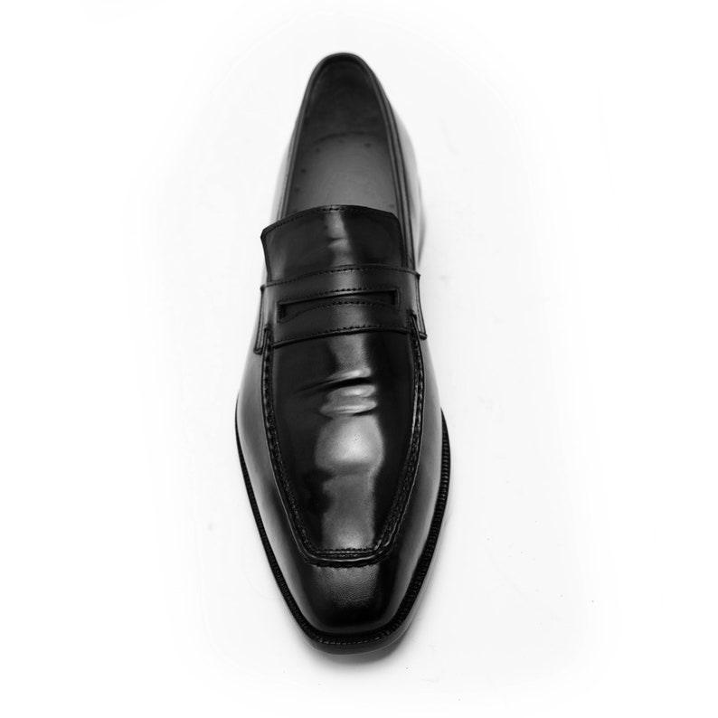 Puede incluir: Un mocas&iacute;n de cuero negro con una tira de penny y una punta puntiaguda.