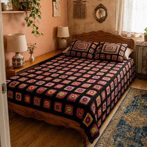 May include: A bedspread and two matching pillow shams featuring a black crochet granny square pattern with vibrant multi-colored centers in shades of red, orange, yellow, pink, and purple, covering a wooden bed frame in a bedroom setting.