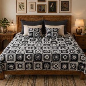 May include: A crochet bedspread and two matching square throw pillows featuring a repeating granny square pattern in shades of black, charcoal gray, light gray, and white, with each square containing a central floral motif design.