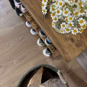 May include: A wooden shoe rack with multiple pairs of shoes on the shelves. A vase of white and yellow daisies sits on the top shelf. A basket filled with firewood is in the foreground.