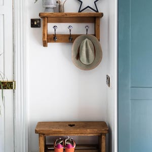 K&ouml;nnte beinhalten: Ein Holz-Kleiderst&auml;nder mit drei Haken und einem Regal. Ein Hut h&auml;ngt an einem der Haken. Ein Holz-Schuhregal mit zwei Regalbrettern befindet sich unter dem Kleiderst&auml;nder. Das Schuhregal hat einen herzf&ouml;rmigen Ausschnitt in der Oberseite.
