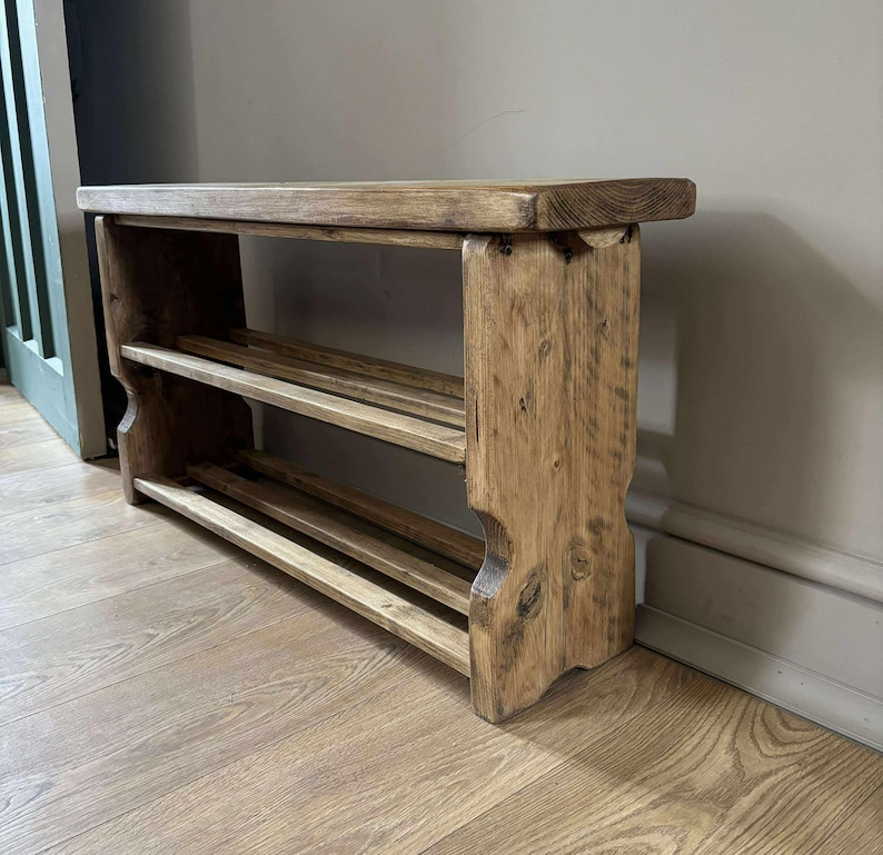 May include: A rustic wooden shoe rack with two shelves and a bench-style top. The natural wood has visible grain and knots, with a warm, light brown color. The rack is designed for entryway storage.