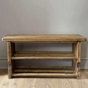 May include: A rustic wooden shoe rack with two slatted shelves and a solid top. The natural wood finish displays visible grain and knots. The shoe rack is approximately 36 inches long, 12 inches deep, and 18 inches high.