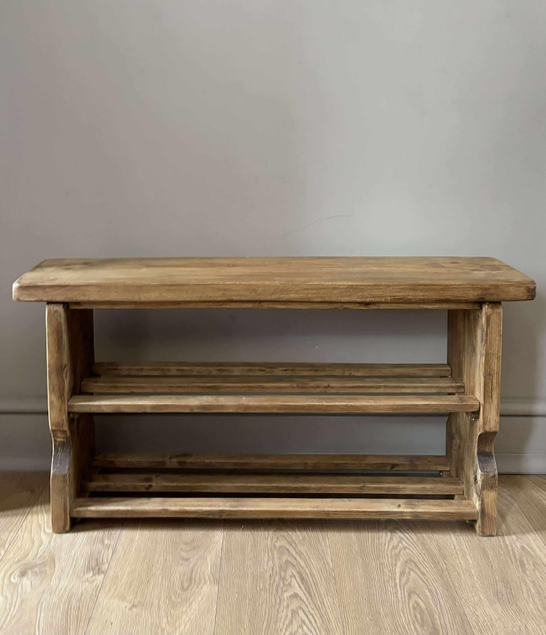 May include: A rustic wooden shoe rack with two slatted shelves and a solid top. The natural wood finish displays visible grain and knots. The shoe rack is approximately 36 inches long, 12 inches deep, and 18 inches high.