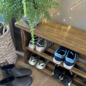 May include: A wooden shoe rack with multiple pairs of shoes, including sneakers and boots. A potted fern sits on top of the rack. A woven basket and a star-shaped light fixture are also visible.
