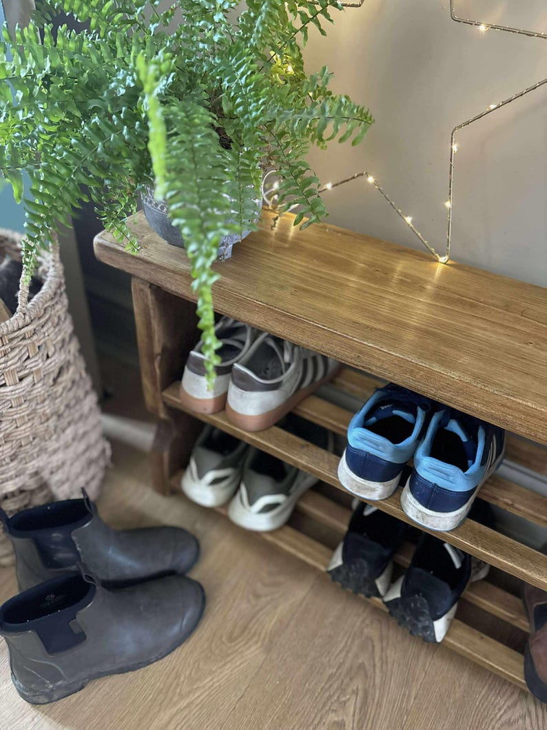 May include: A wooden shoe rack with multiple pairs of shoes, including sneakers and boots. A potted fern sits on top of the rack. A woven basket and a star-shaped light fixture are also visible.