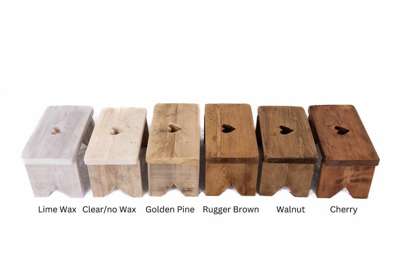 May include: Six small wooden stools in various finishes, including lime wax, clear wax, golden pine, rugger brown, walnut, and cherry. Each stool has a heart-shaped cutout on the top surface. The stools are displayed against a white background.