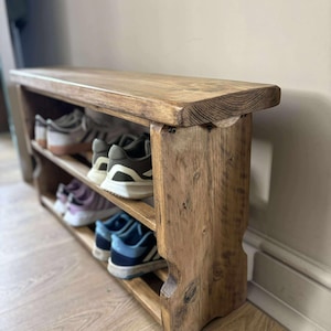 May include: A rustic wooden shoe rack with three shelves and a bench seat. The rack is made of light brown wood and holds several pairs of shoes. The design is simple and functional, perfect for an entryway or mudroom.