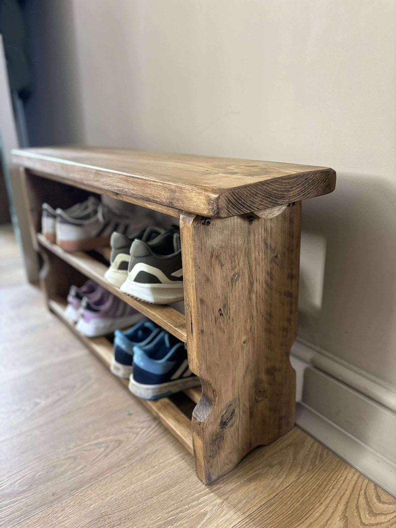May include: A rustic wooden shoe rack with three shelves and a bench seat. The rack is made of light brown wood and holds several pairs of shoes. The design is simple and functional, perfect for an entryway or mudroom.