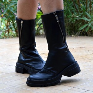 K&ouml;nnte beinhalten: Schwarze Lederstiefel mit einer dicken Plateau-Sohle und einem Rei&szlig;verschluss an der R&uuml;ckseite des Stiefels.