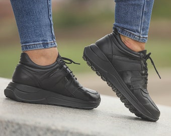 May include: A pair of black leather sneakers with a thick white sole. The sneakers have a lace-up closure and a sporty design.