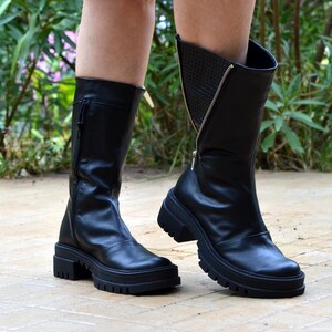 K&ouml;nnte beinhalten: Schwarze Lederstiefel mit einer dicken Plateau-Sohle und einem Rei&szlig;verschluss an der Seite. Die Stiefel haben ein strukturiertes Detail an der R&uuml;ckseite des Kn&ouml;chels.