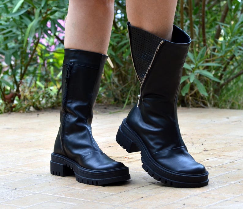 K&ouml;nnte beinhalten: Schwarze Lederstiefel mit einer dicken Plateau-Sohle und einem Rei&szlig;verschluss an der Seite. Die Stiefel haben ein strukturiertes Detail an der R&uuml;ckseite des Kn&ouml;chels.