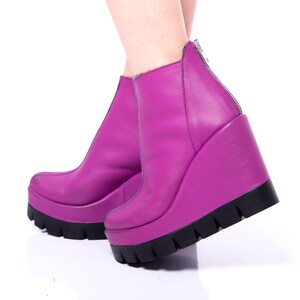 May include: A pair of purple wedge heeled ankle boots with a zipper on the back. The boots are made of leather and have a chunky platform.